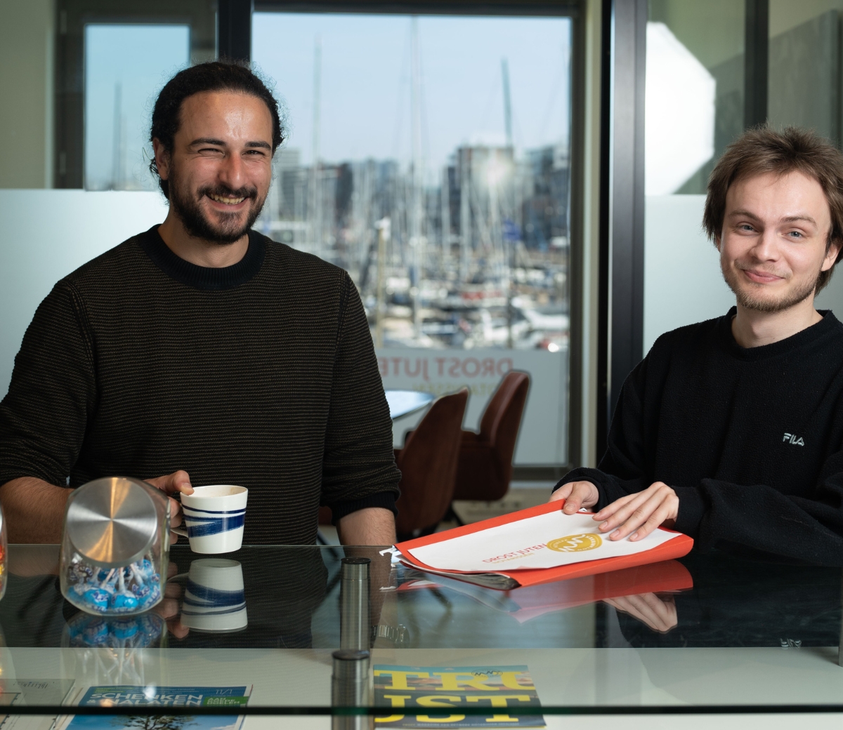 2 mannen voor een raam op kantoor met de haven op de achtergrond